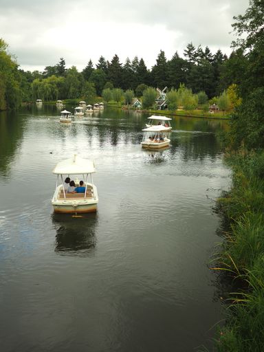 A vertical shot of people riding in white small boats in the lake surrounded by green plants with a cloudy gloomy sky