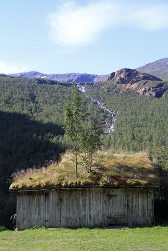 A vertical shot of a wooden house near a forested mountain under a blue sky