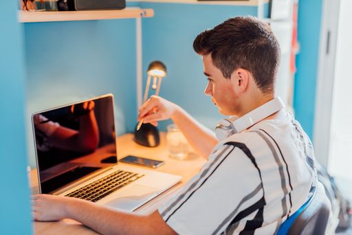 A teen studying with a laptop in his room. Concept online class.