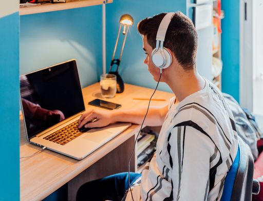 A teen studying with laptop and headphones in his room. Concept online class.