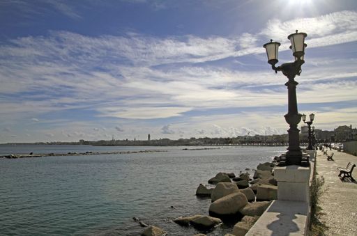 A street lantern near a sea with buildings in the distance under a blue sky