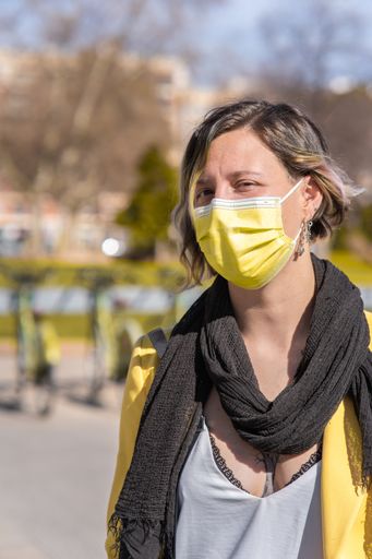 A vertical shot of a Spanish woman wearing a yellow face mask outdoors