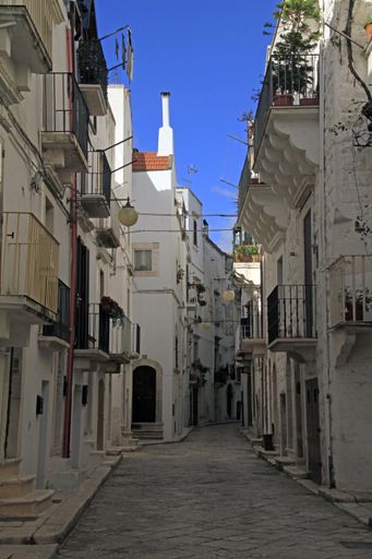 A vertical shot of a pathway in the middle of white buildings under a blue sky