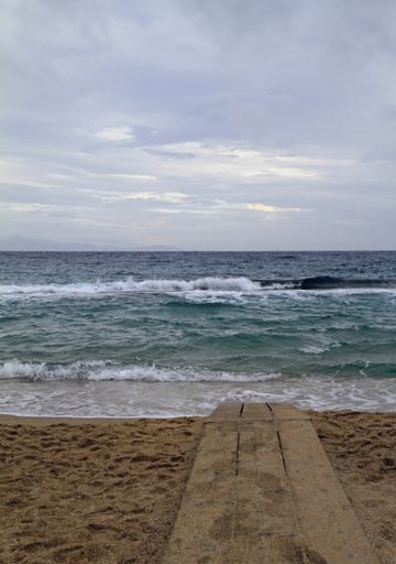 A vertical shot of a wooden pathway towards the beach under a cloudy sky