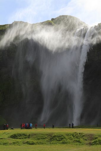A vertical shot of people standing near the waterfall at daytime