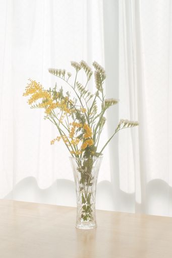 A vertical shot of delicate freshly picked summer flowers in a transparent vase indoors