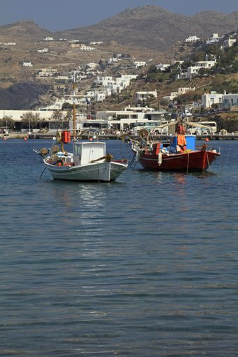 A vertical shot of two boats on the water with buildings in the distance near the mountains