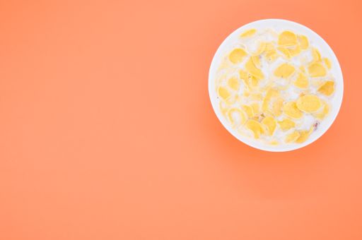 A closeup shot of a small white bowl with milk and sweet cornflakes isolated on orange background