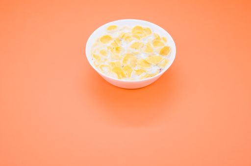 A closeup shot of a small white bowl with milk and sweet cornflakes isolated on orange background