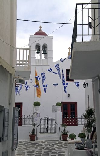 A vertical shot of a white bell tower with the Greece flags attached to ropes