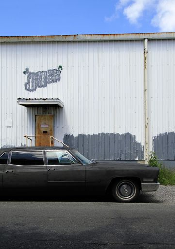 A vertical shot of a black vintage car parked near a white building