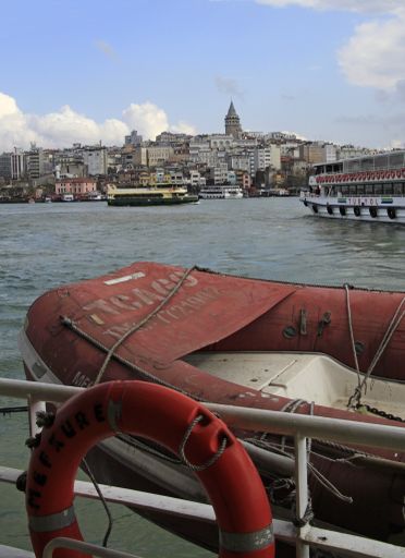 A vertical shot of a red boat on the water with buildings in the distance