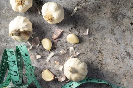 The peeled garlic heads and cloves on a grey stone next to a tape measure. Concept of healthy food with vitamins.