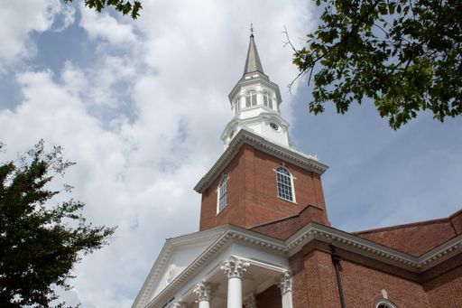 A low angle shot of a high stone structure's steeple with cloudy sky in the background