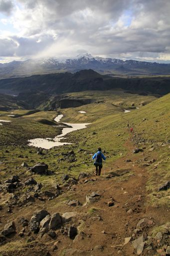 A vertical shot of a person hiking on the mountains under a cloudy sky