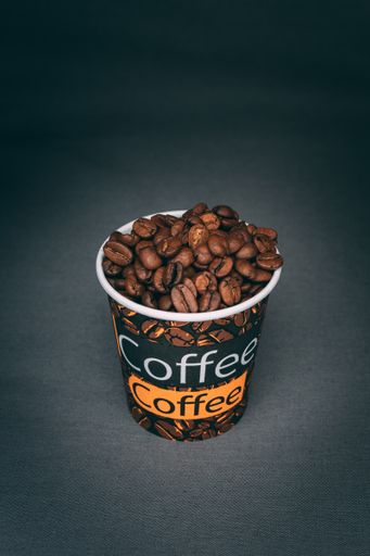 A vertical shot of a printed cup full of roasted coffee beans isolated on dark background