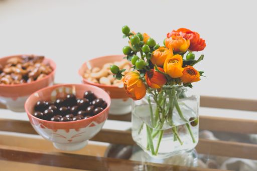 A closeup of colorful flowers in a small glass jar with different types of sweets in bowls on the side