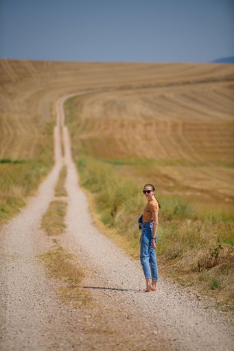 A vertical shot of a young female standing on a path in the field
