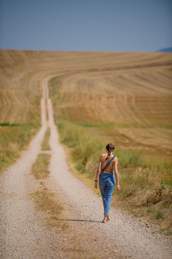 A vertical shot of a young female standing on a path in the field