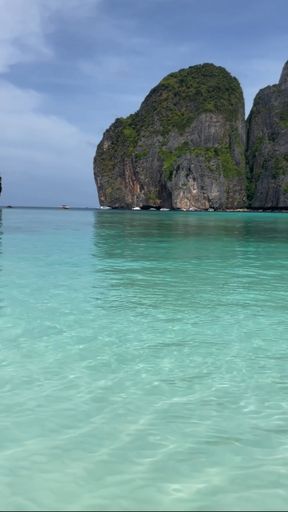 A majestic large mossy rock formation set against the backdrop of a stunning crystal clear sea