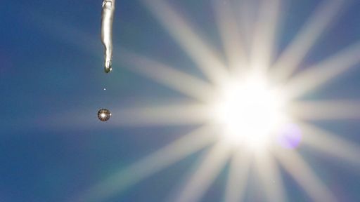 frozen icicle melts in the winter sun, climate change symbol image, light blue sky and midday sun. Climate change, global warming