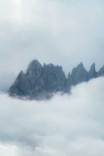 A vertical shot of the Dolomites Mountain Range covered in the fog under a cloudy sky in Italy