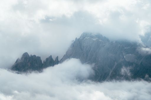 A landscape of the Dolomites Mountain Range covered in the fog under a cloudy sky in Italy