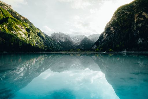 A landscape of the Durrensee lake surrounded by rocky hills under a cloudy sky and sunlight in Italy