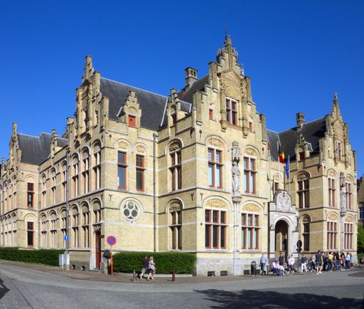 Town hall of Ypres (Ieper) in Flanders, Belgium, with people around the front of the building, enjoying the evening sunshine and blue, cloudless sky.