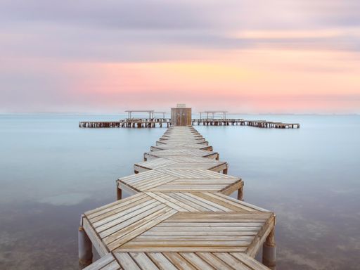 Wiew of a wooden pier in Mar Menor lagoon, from Los Alcazares, Murcia, Spain at dawn. A long boardwalk on the calm water of the lake at dusk.