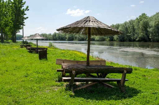 A scenic outdoor setting featuring parasols and benches by the river Bosut