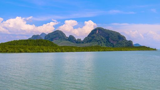 A mesmerizing view of an island covered in greens on the ocean against the cloudy blue sky