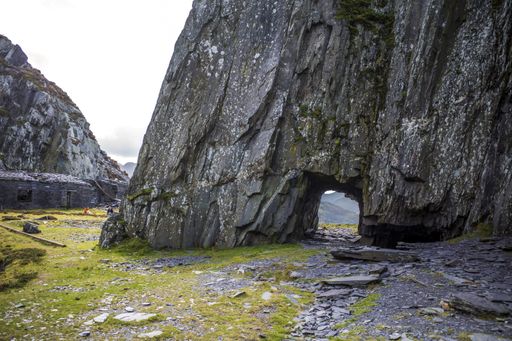 An arch through rocky mountain covered in moss in Dinorwig quarry, Llanberris, North Wales