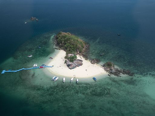 An aerial shot of a small island with a few buildings and boats and a blue dock