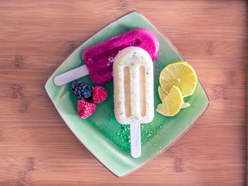 A high angle shot of two delicious popsicles with fruits in a green plate on a wooden table