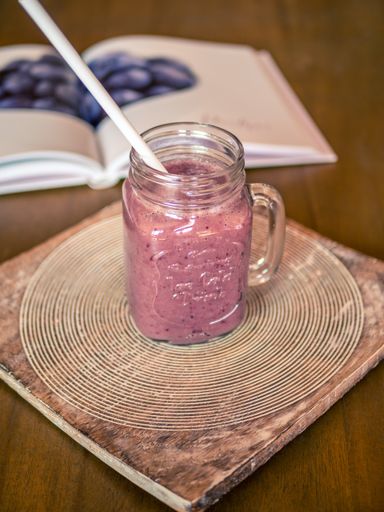 A vertical closeup shot of a berry smoothie in a mason jar with a straw on a tray