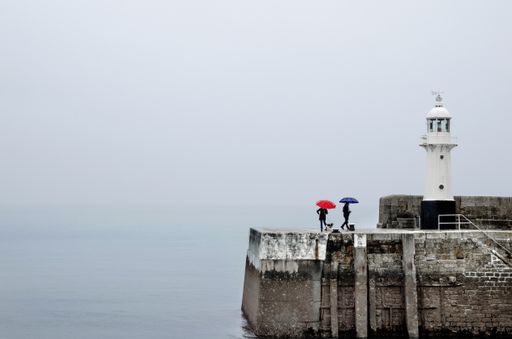 A white lighthouse with people walking near it during a cloudy day