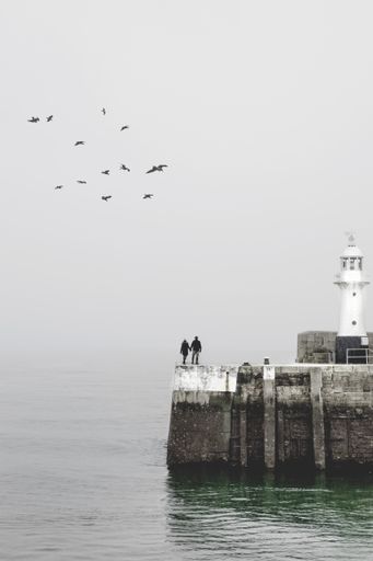 A vertical shot of a white lighthouse with people walking near it during a cloudy day