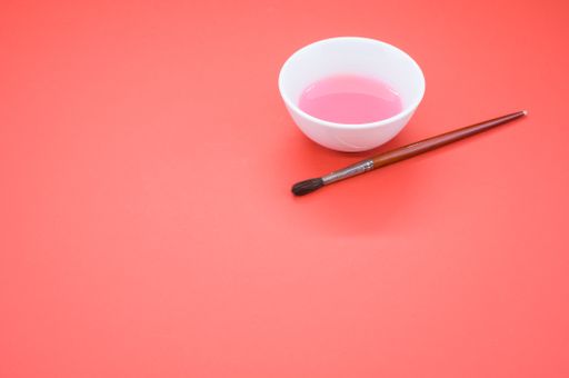 A closeup shot of a brush with a pink paint bowl on an orange background