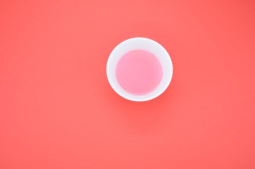 An overhead shot of a bowl of pink paint on an orange background