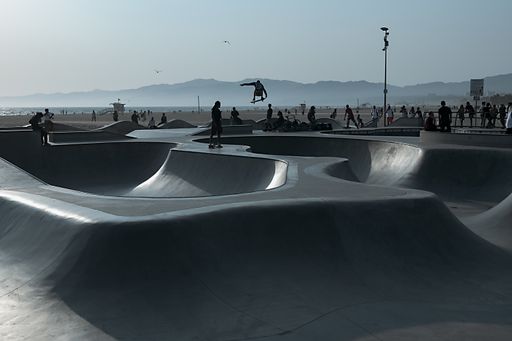 A selective focus shot of several unrecognizable skateboarders showing different tricks at the skate park by the ocean of Venice Beach at the sunset