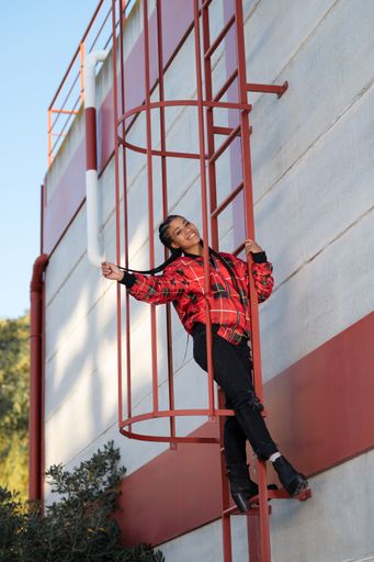 A vertical shot of a smiling black girl on a red escape ladder outdoors