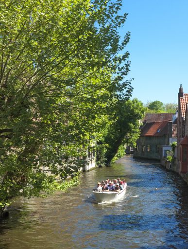 Canal in the old historic district of Bruges (Brugge) Belgium, with old houses  and a cruise-boat containing tourists also visible