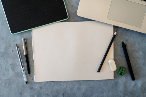 A top view of blank drawing sheet with pencils, pens and graphic tablet