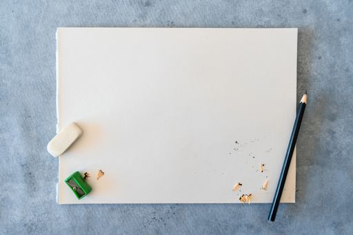A top view of blank drawing sheet with a sharp pencil, sharpener and eraser