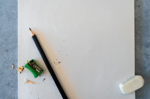 A top view of blank drawing sheet with a sharp pencil, sharpener and eraser