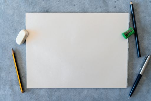 A top view of blank drawing sheet with pencils, pen, sharpener and eraser