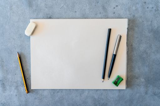 A top view of blank drawing sheet with pencils, pen, sharpener and eraser