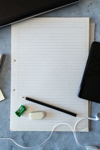 A top view of a blank sheet with smartphone, earphones, pencil, eraser and sharpener
