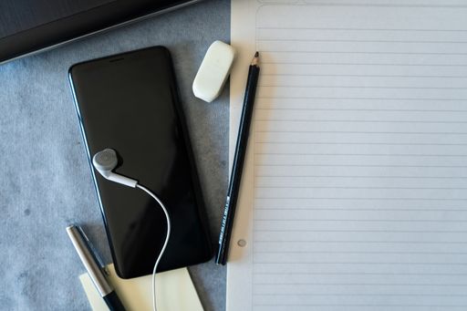 A top view of a blank sheet with smartphone, earphones, pen, pencil and eraser